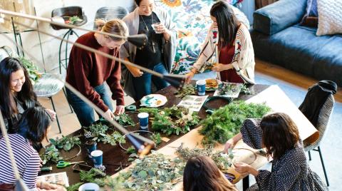 Six people are gathered around a table working on crafts