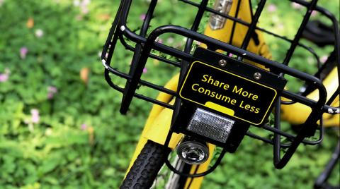 Yellow bike on green grass with a sign that says 'Share more, consume less'