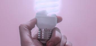 A hand holds up a lit low energy bulb.