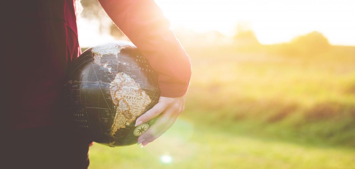 Person Holding a Globe to their side while sunshines in the background