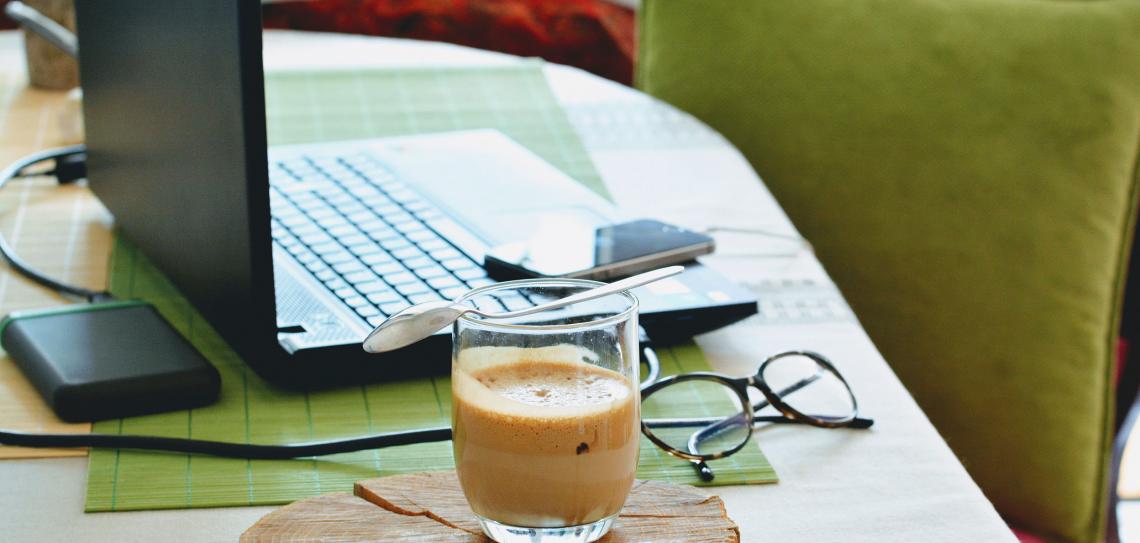 Coffee sitting next to a laptop on a desk with a green chair in the background.