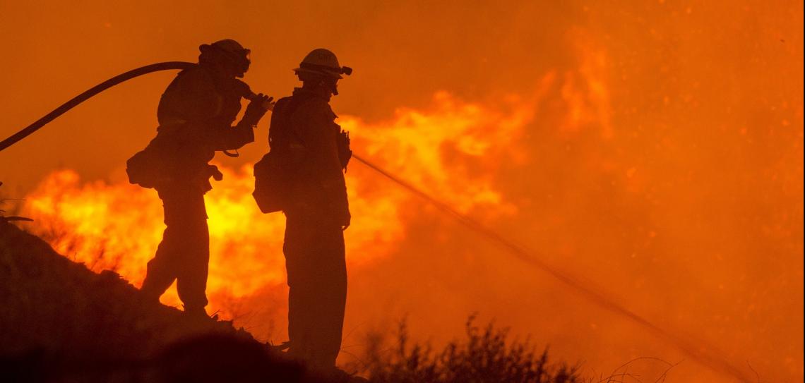 Firefighters use a hose to control a wildfire
