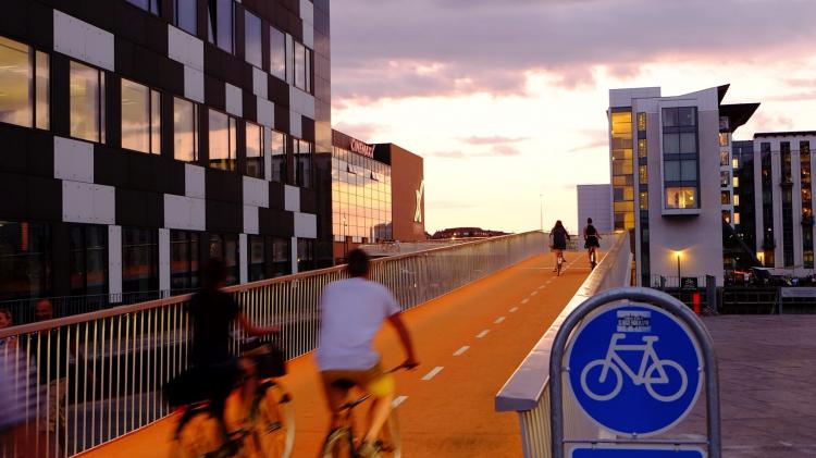 Cyclists cross a cycle bridge by a tall office block
