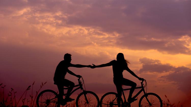 Two people on bikes riding bikes with a orange and pink sunset in the background