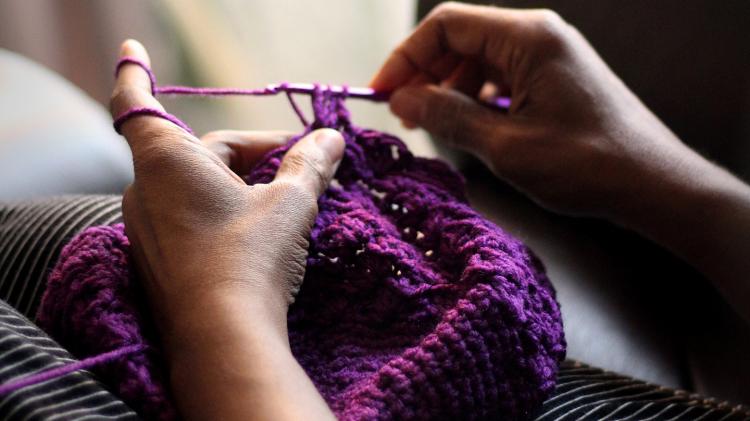 Hands knitting a purple hat