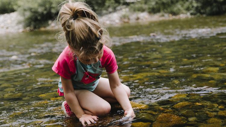 Child kneeling in a river looking at the water